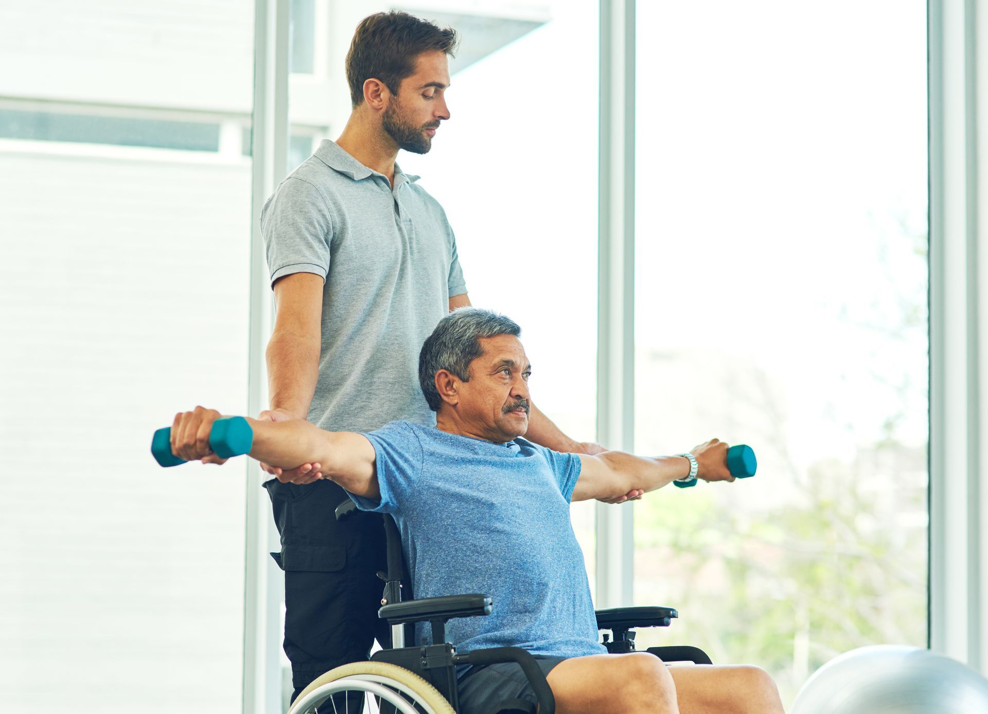A man in a wheelchair is doing exercises with dumbbells.
