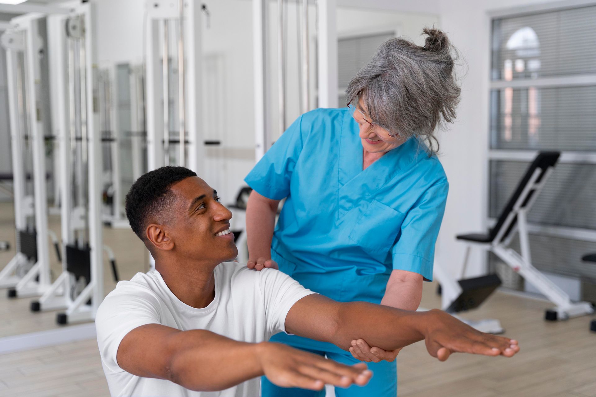 A nurse is helping a man stretch his arms in a gym.