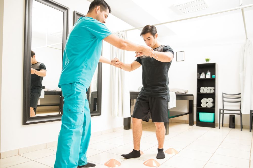 A nurse is helping a man with his exercises in a gym.