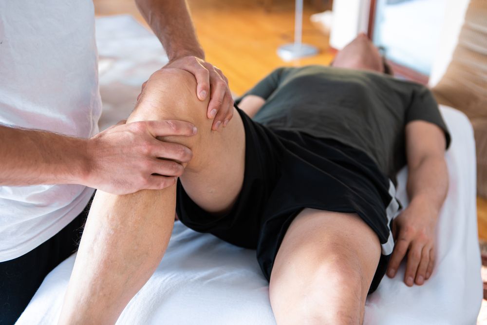 A man is laying on a bed getting a massage on his knee.