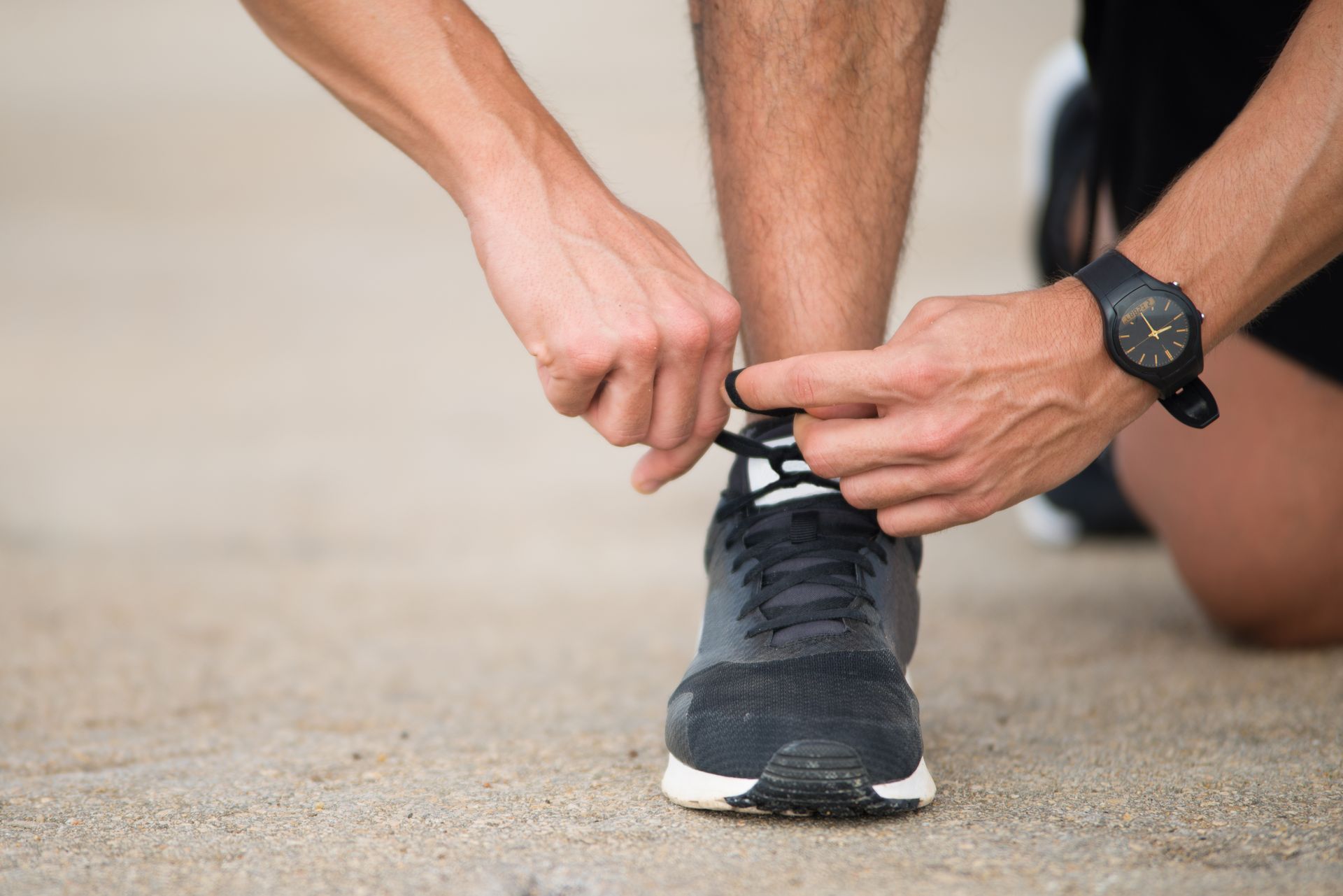 A man is tying his shoes while wearing a watch.