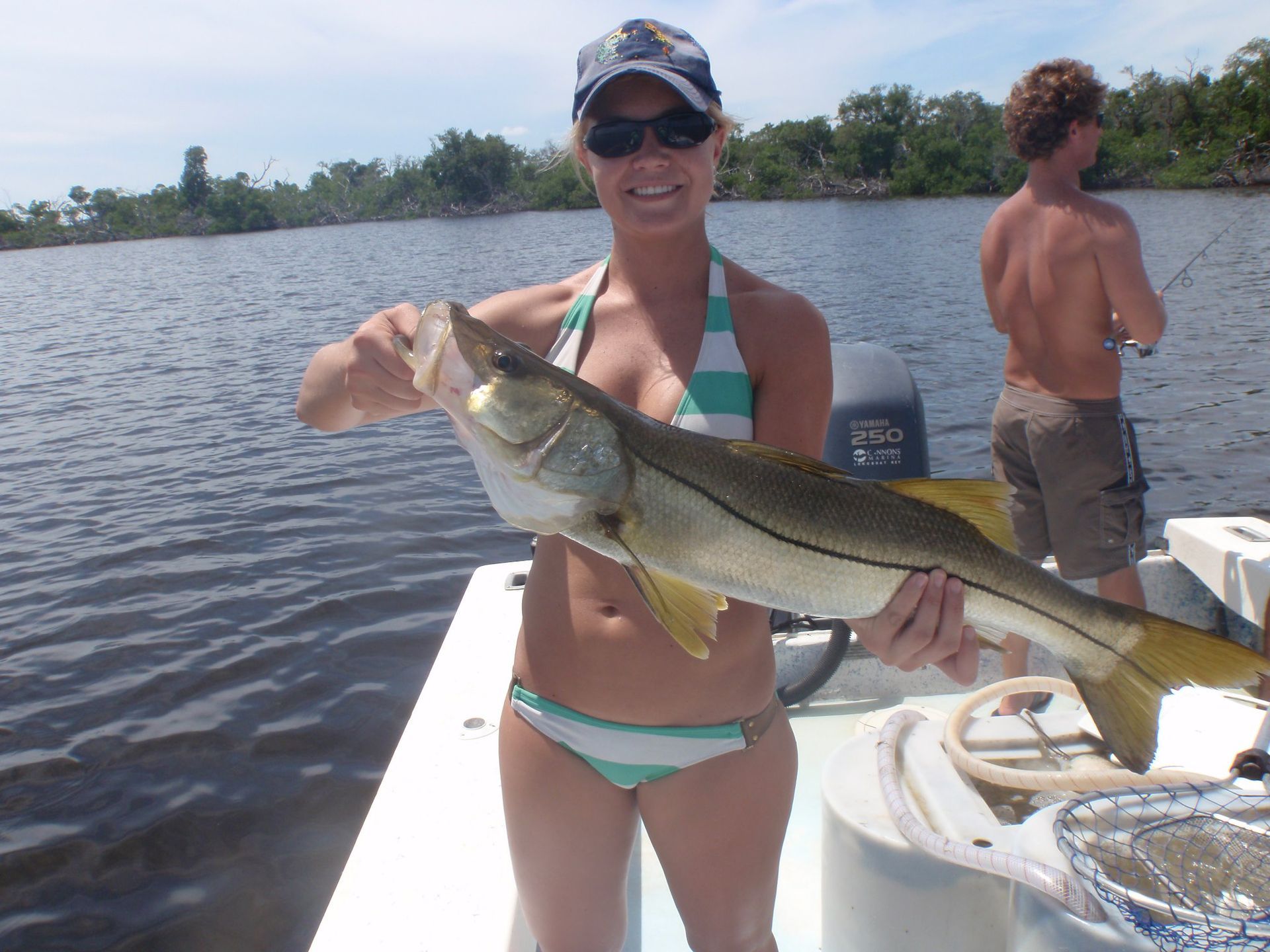 A woman in a bikini is holding a large fish on a boat
