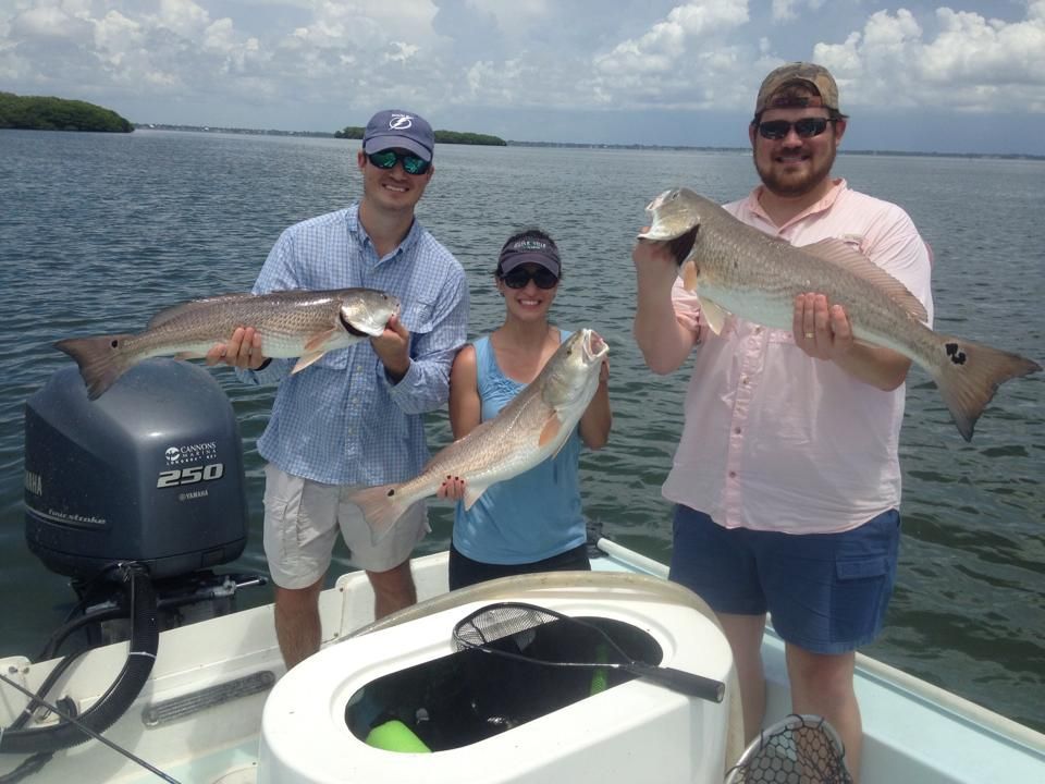Three people are standing on a boat holding fish.