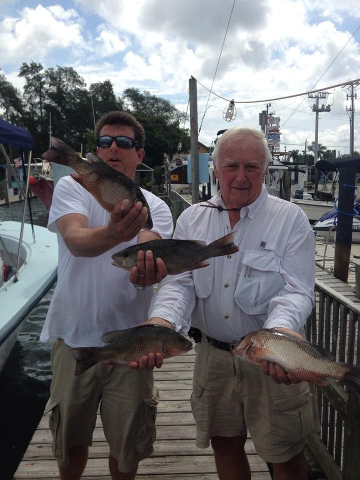 Two men standing on a dock holding fish in their hands