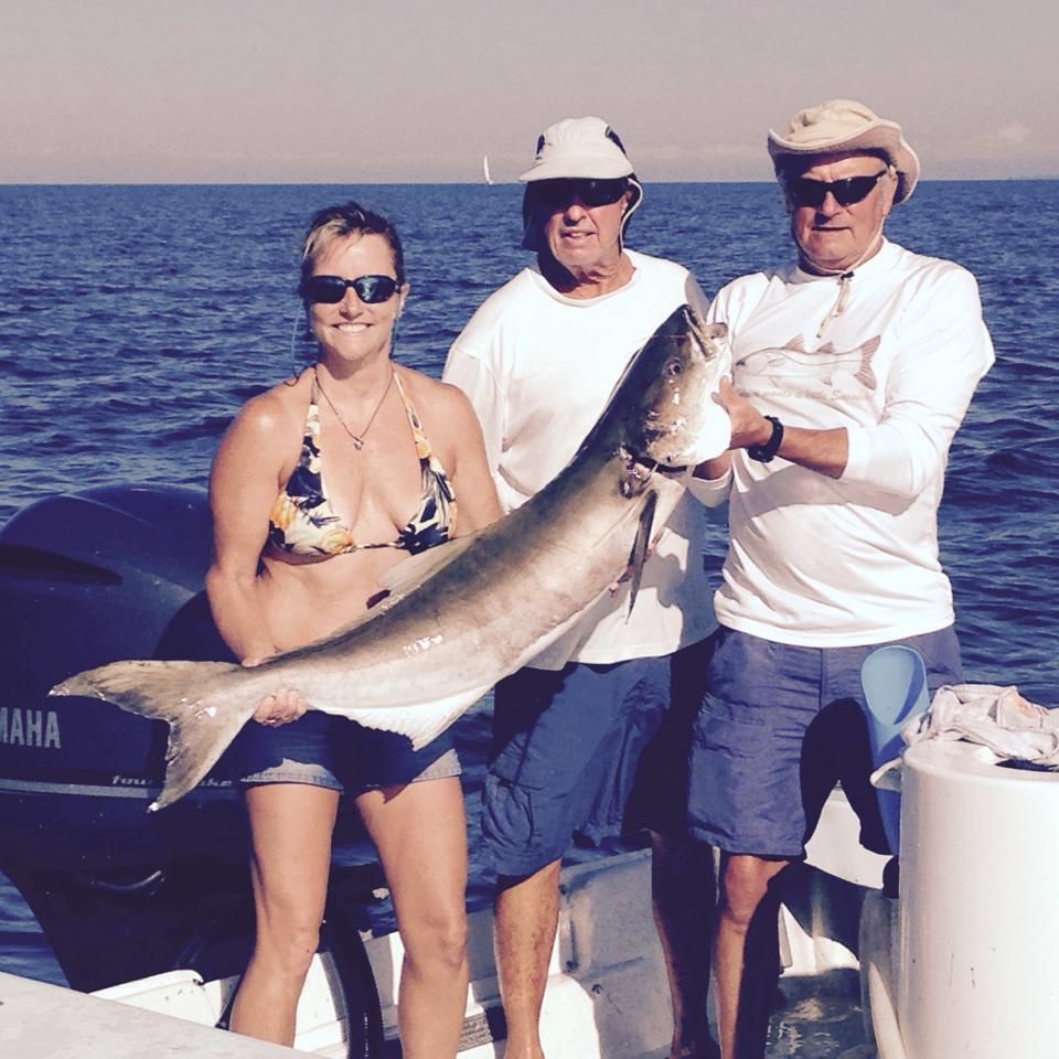 A woman in a bikini is holding a large fish in front of a yamaha boat