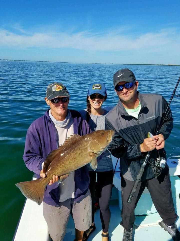 Three people are standing on a boat holding a large fish.