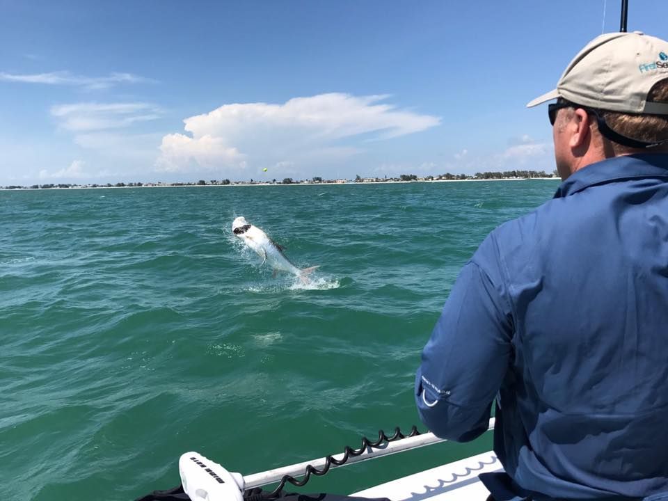 A man is standing on a boat looking at a fish jumping out of the water.