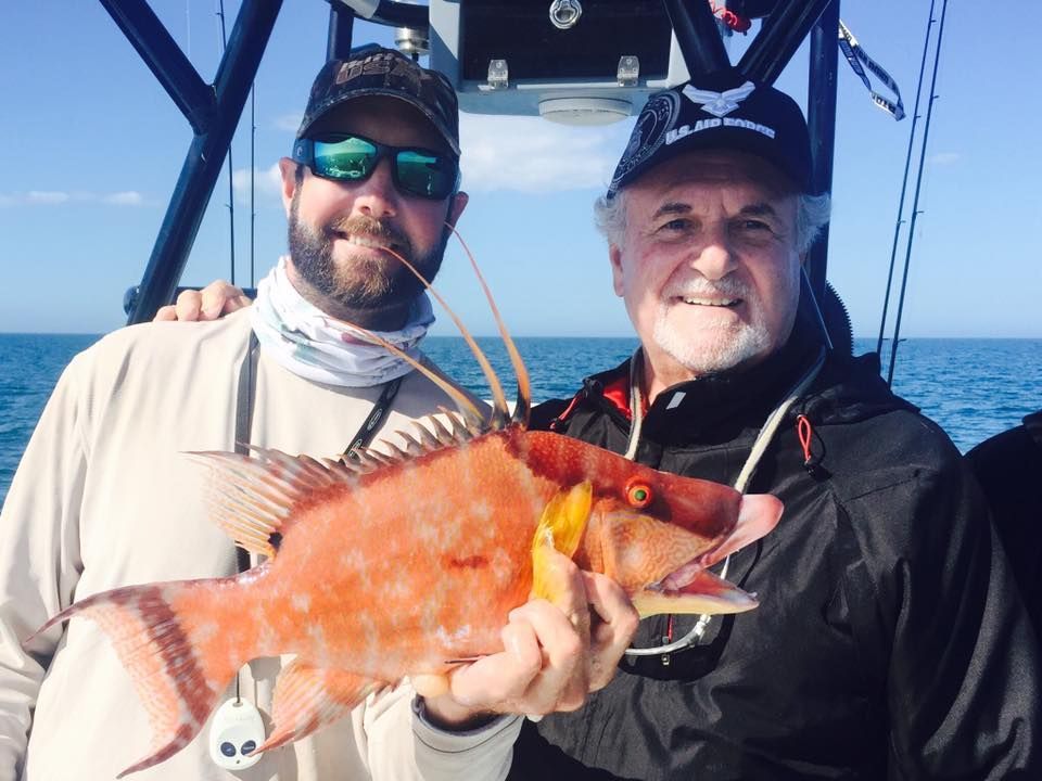 Two men are holding a large red fish on a boat.