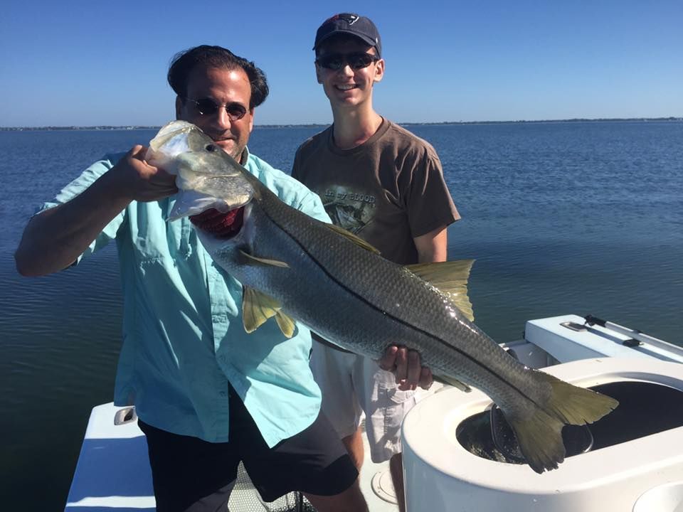 Two men are standing on a boat holding a large fish