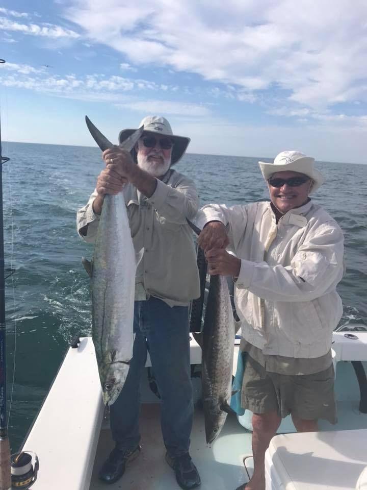 Two men are holding fish on a boat in the ocean.