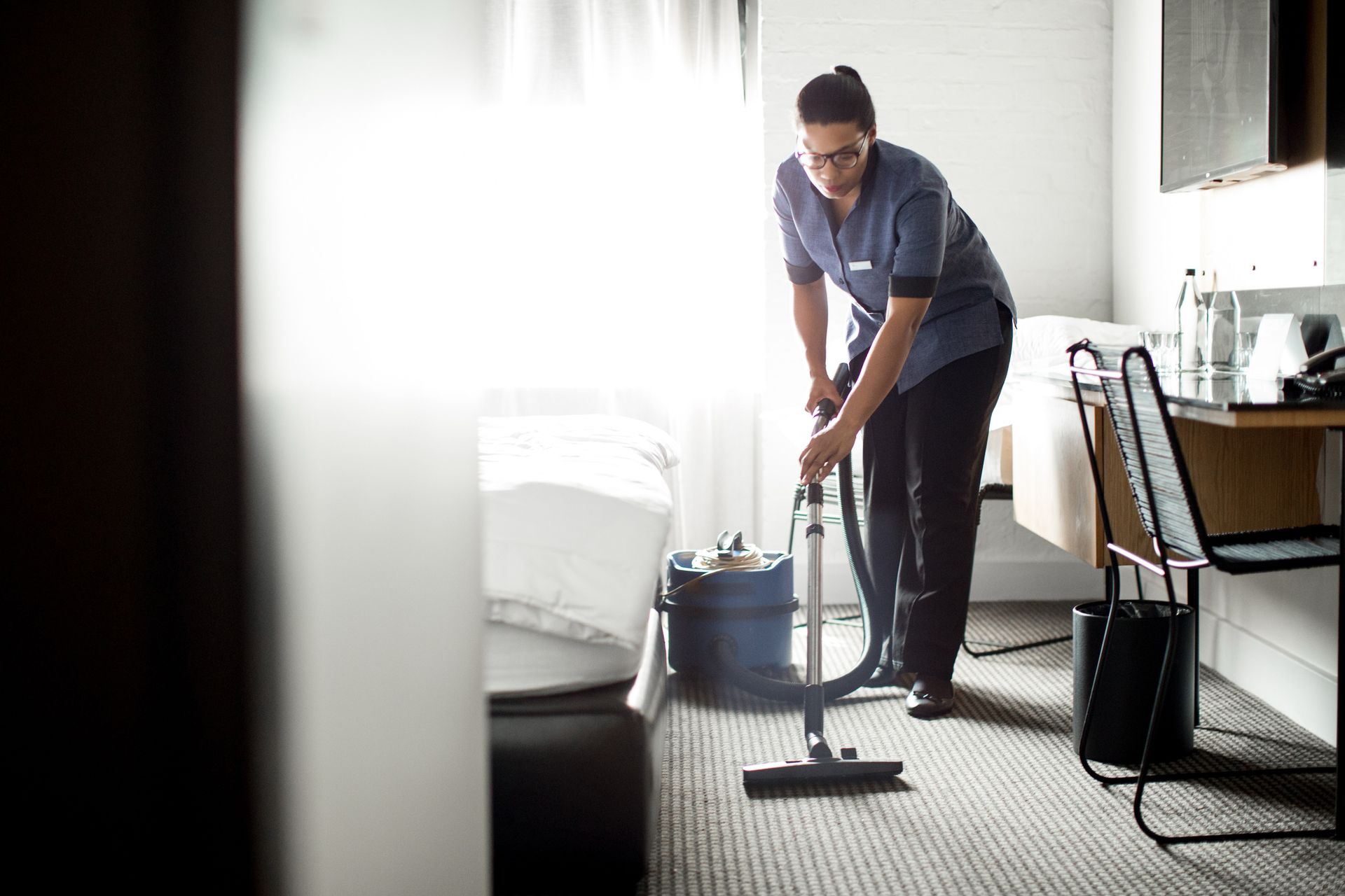 Lady vacuuming the carpet in a hotel room.