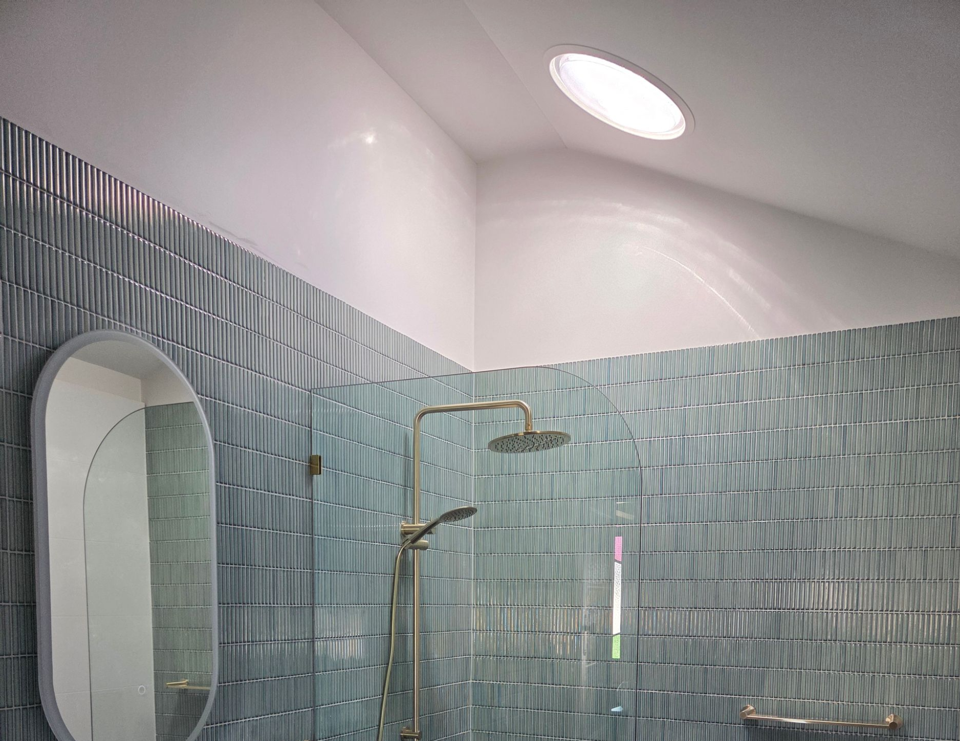 Modern bathroom with blue textured tile, oval mirror, floating vanity, and black hexagonal floor tiles — Beyond Skylights in Byron Bay, NSW
