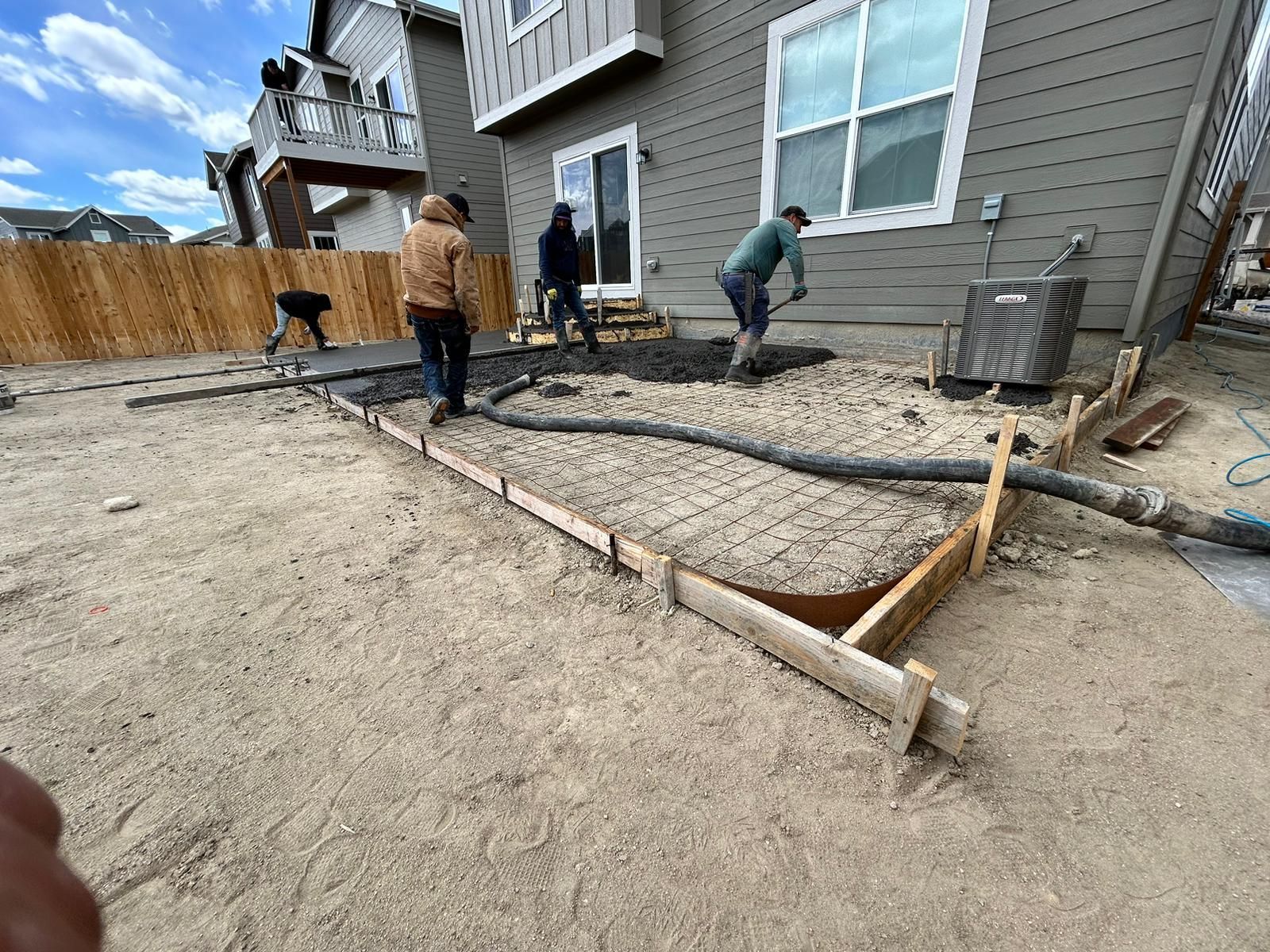 A group of people are working on a concrete patio in front of a house.