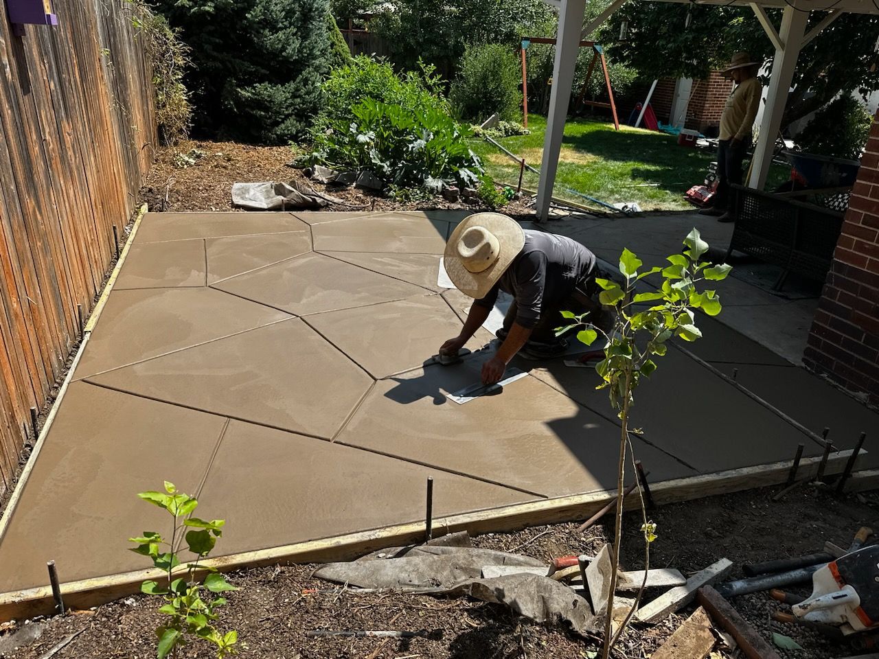 A man wearing a hat is working on a concrete patio.