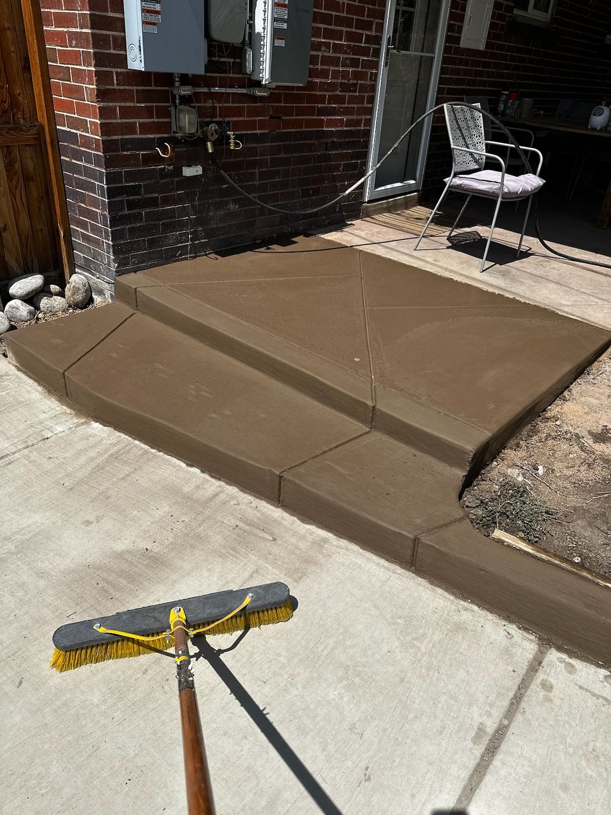 A broom is sitting on the sidewalk in front of a brick building.