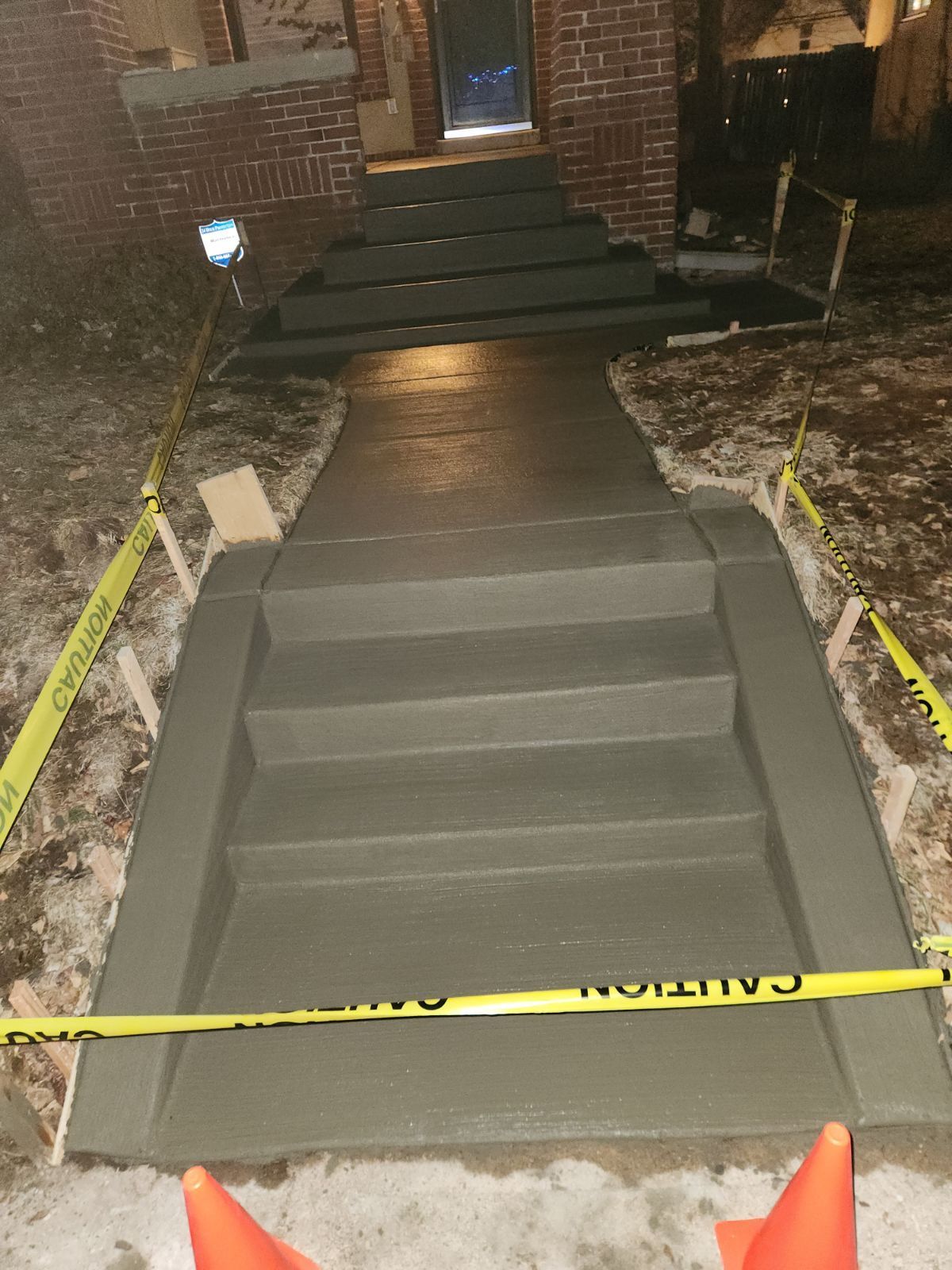 A concrete walkway is being built in front of a brick house