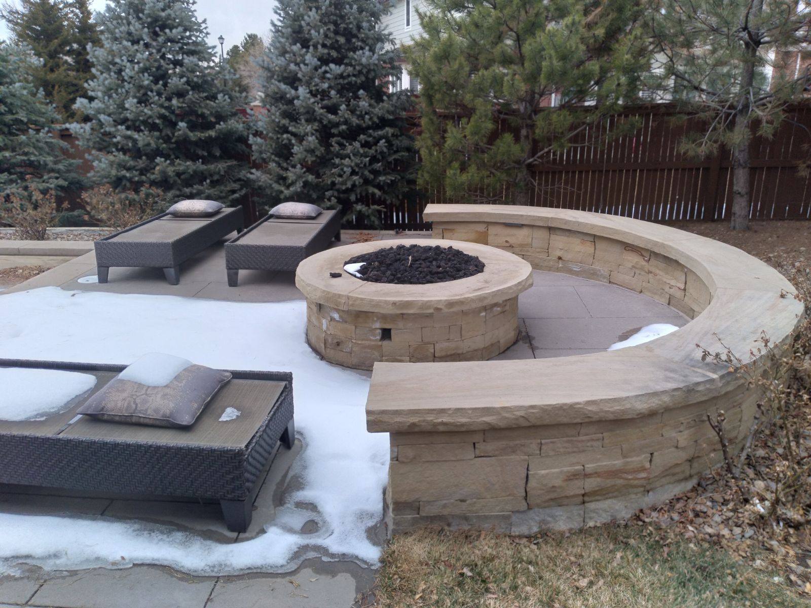 A fire pit in the middle of a patio with snow on the ground