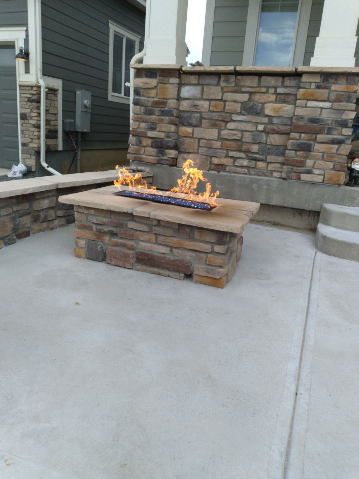 A fire pit is sitting on a concrete patio in front of a stone wall.