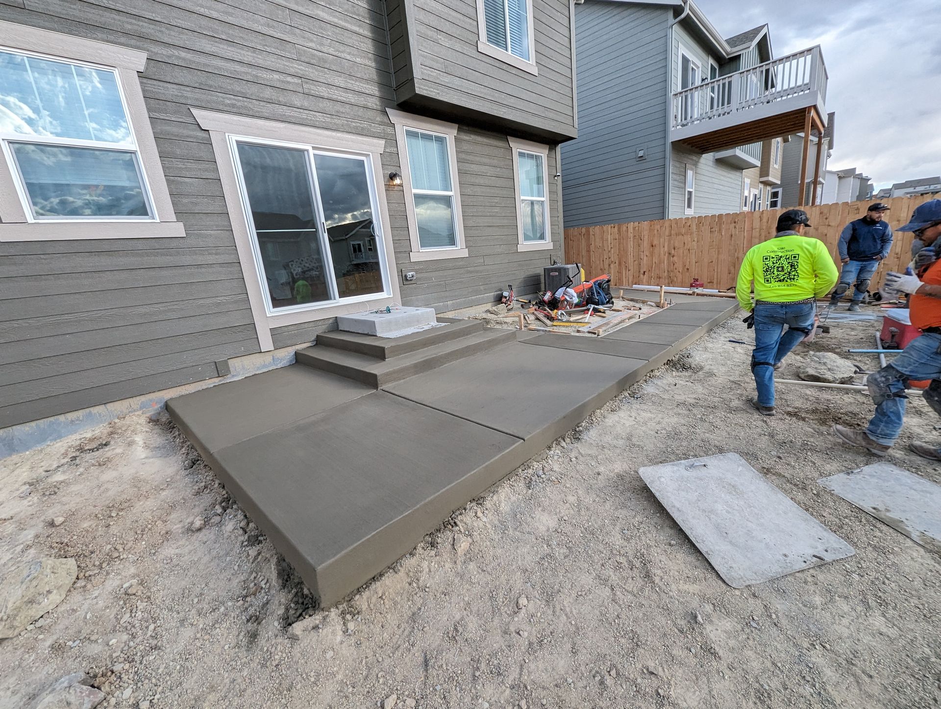 A group of men are working on a concrete walkway in front of a house.