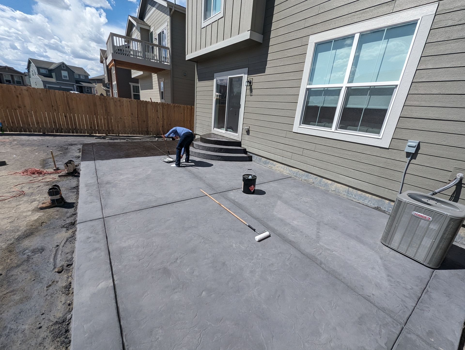 A man is painting a concrete patio in front of a house.