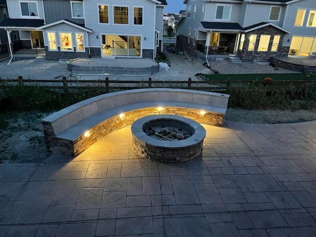 A fire pit with a bench surrounding it is lit up at night.