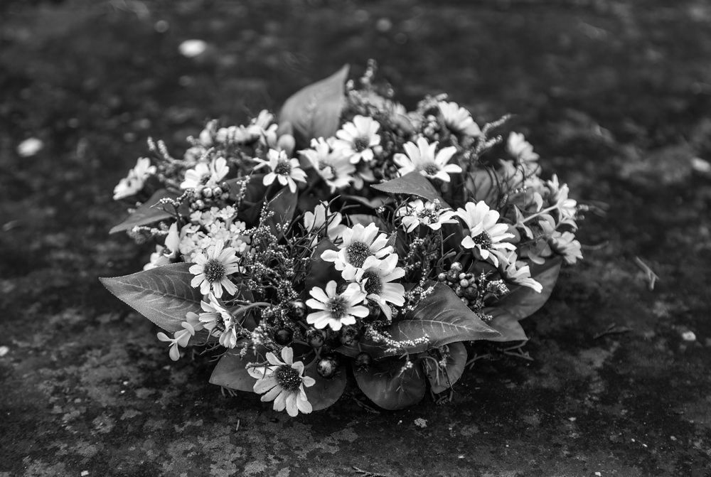 A small, round bouquet of white flowers and green leaves rests on a dark, textured surface.
