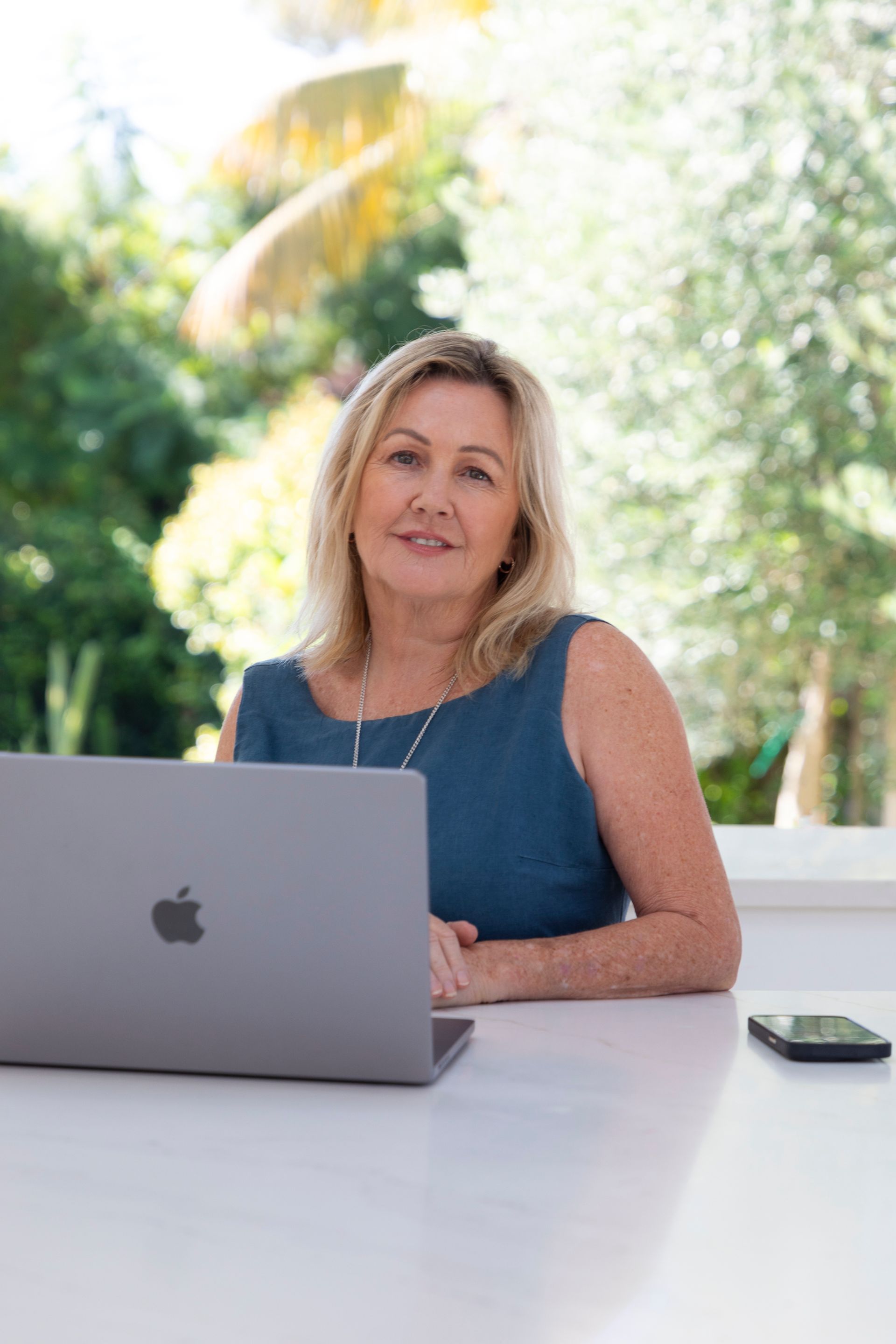 Woman in blue dress using a laptop outside on a white table.