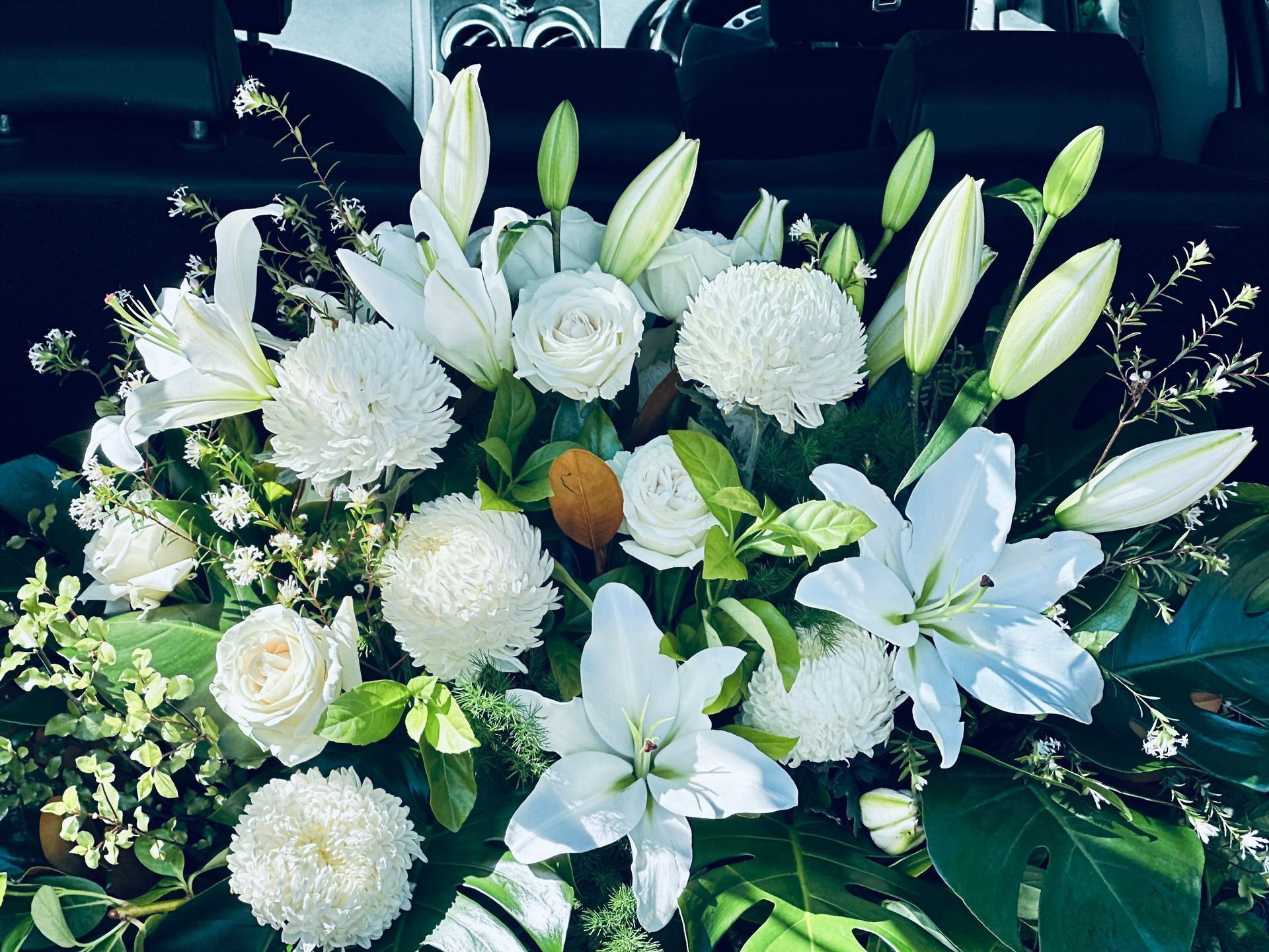 White floral arrangement with lilies, roses, and chrysanthemums, in a car.