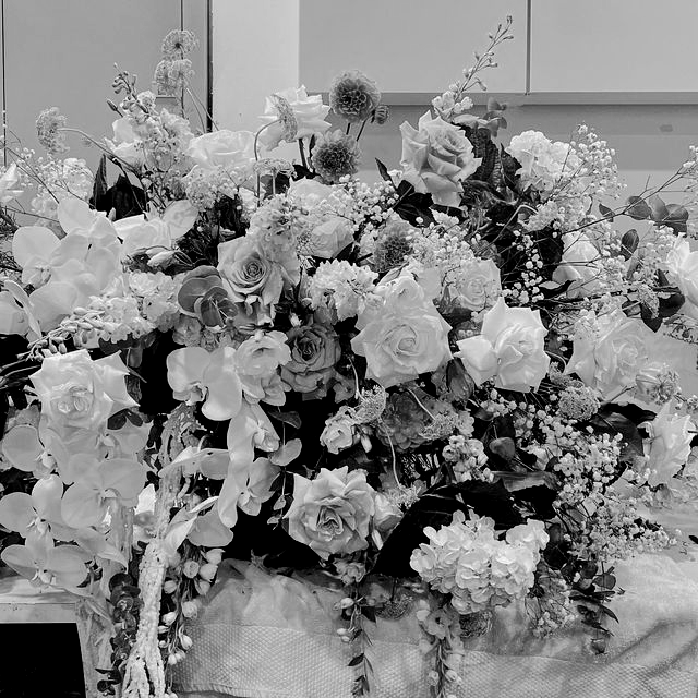 Black and white photo of a large floral arrangement, including roses and orchids, on a table.
