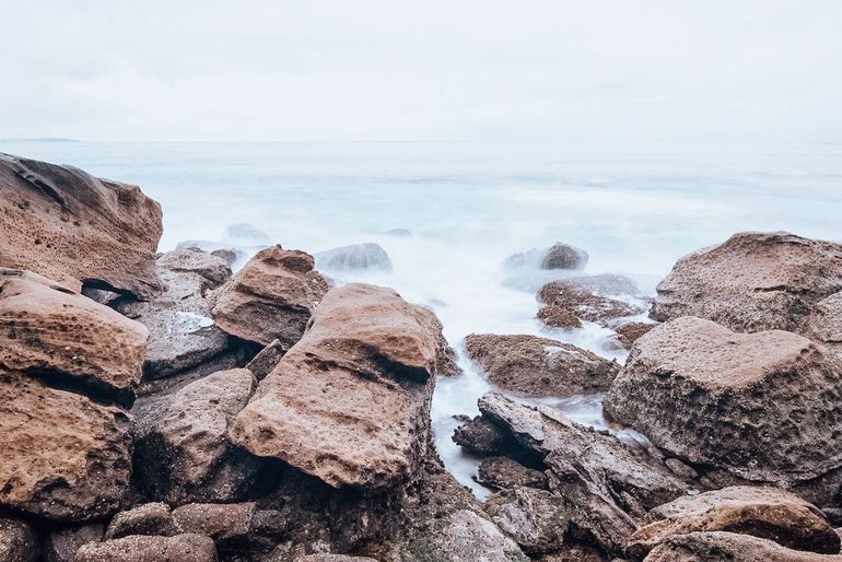 Rocky coastline with blurred water, overcast sky.