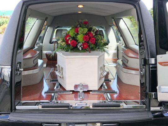 Rear view of hearse, white casket with floral arrangement inside.