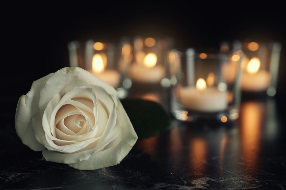 White rose with candles in soft focus, set on a dark, reflective surface.