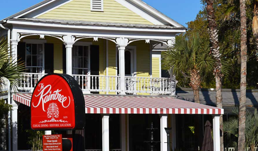 A yellow house with a red and white awning and a sign that says raintree