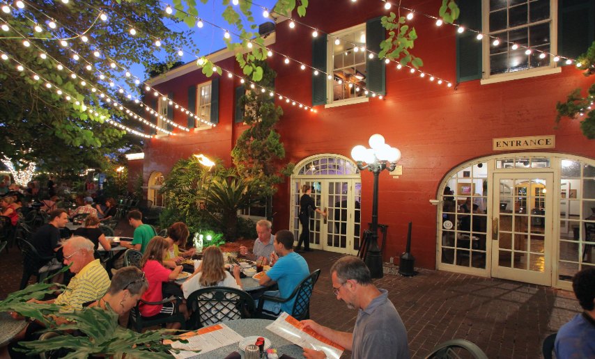 A group of people are sitting at tables outside of a restaurant.