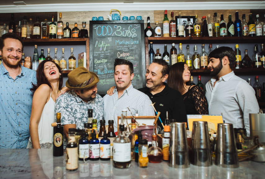 A group of people are posing for a picture in front of a bar filled with bottles of alcohol.