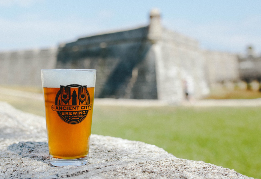 A glass of beer is sitting on a rock in front of a castle.