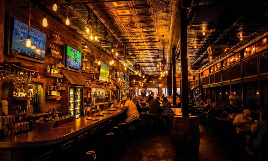 A bar with a lot of people sitting at the bar and tables.