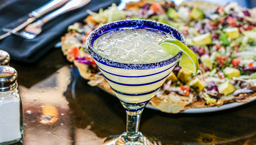 A margarita is sitting on a table next to a plate of food.