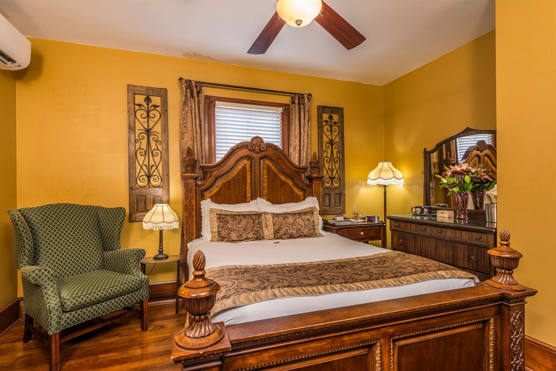 A bedroom with a bed , chair , dresser , mirror and ceiling fan.