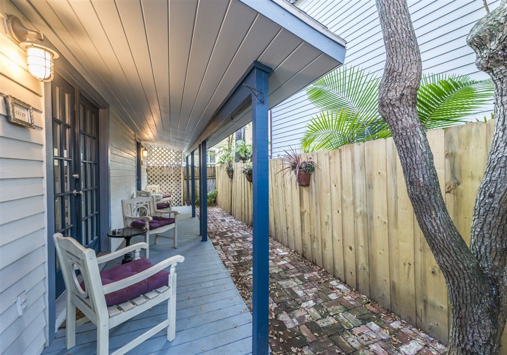 A porch with chairs and a table in front of a wooden fence.