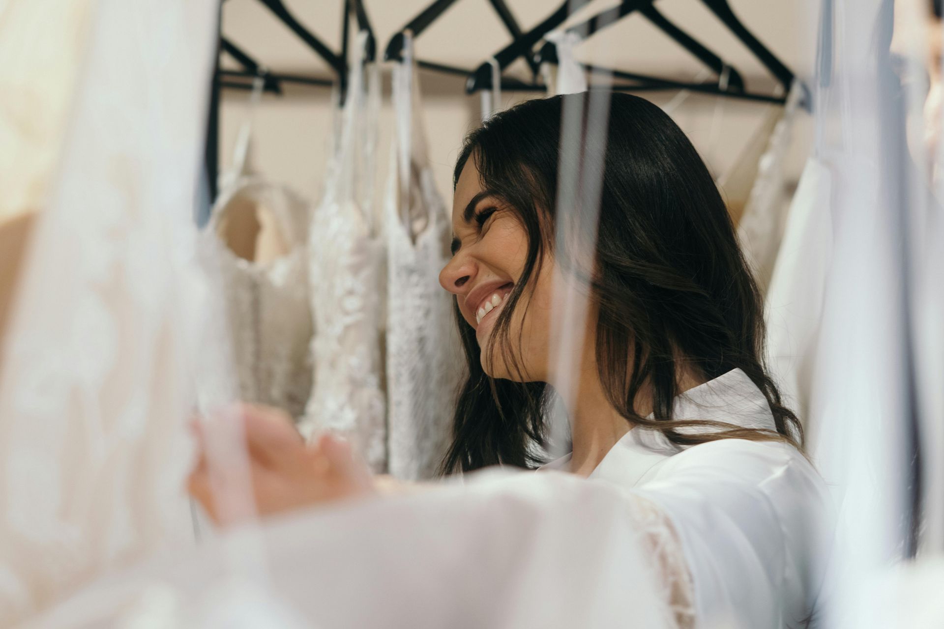 A woman is smiling while looking at wedding dresses in a closet.