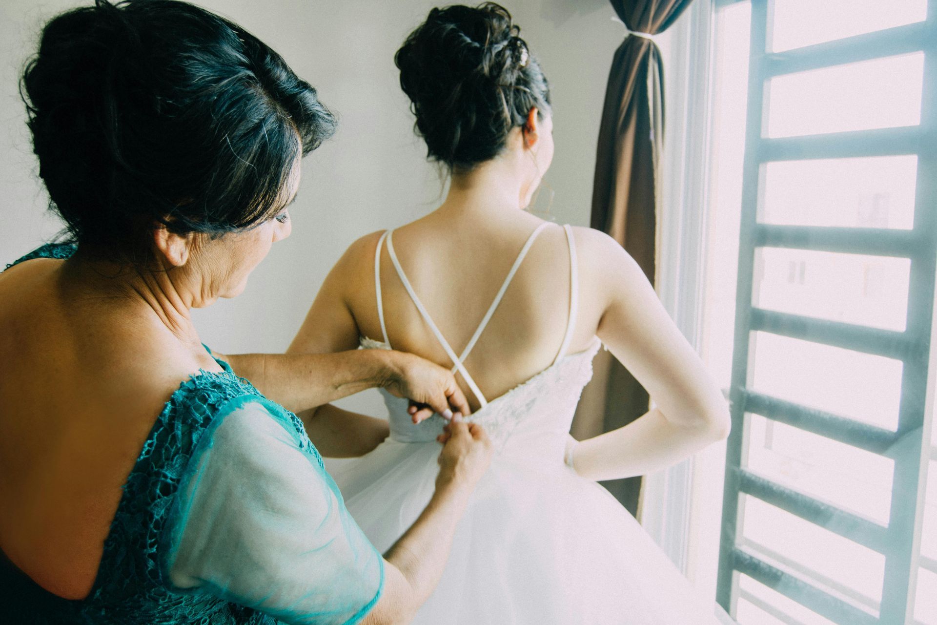 A bride and her mother are holding hands and kissing in a room.