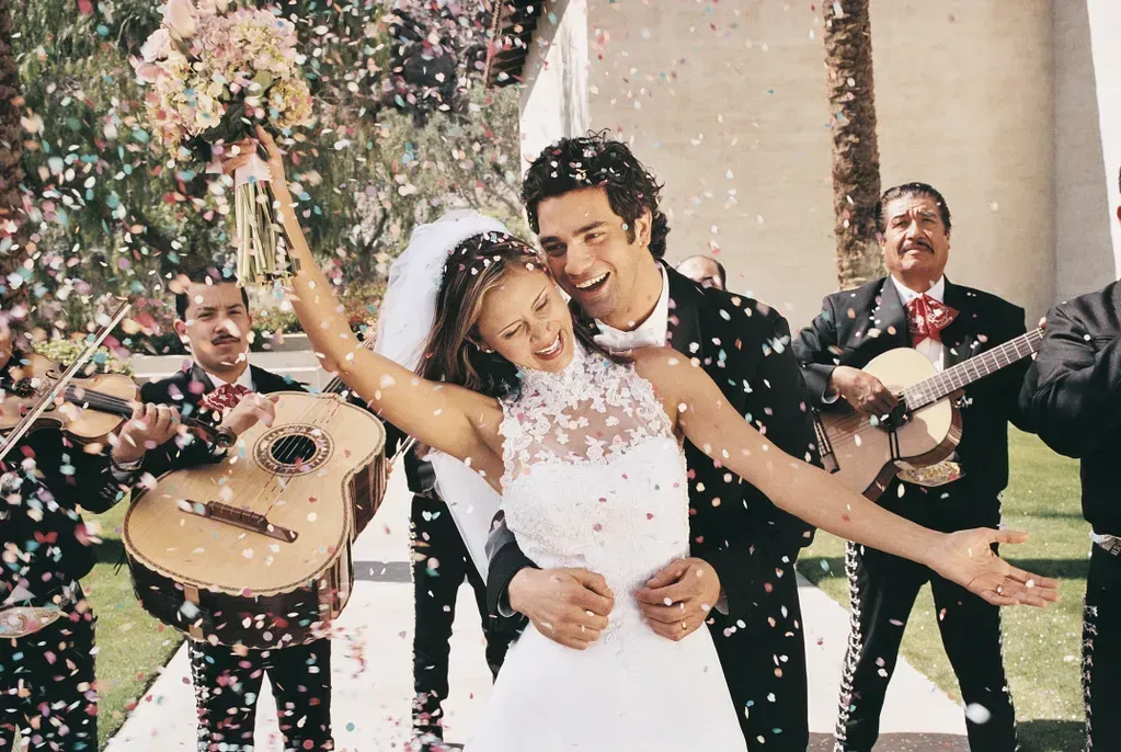 A bride and groom are being showered with confetti by mariachi players