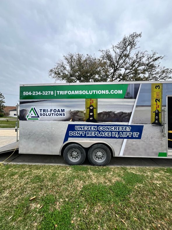 A trailer for Tri-Foam Solutions with company logo and contact info parked on a grassy area.