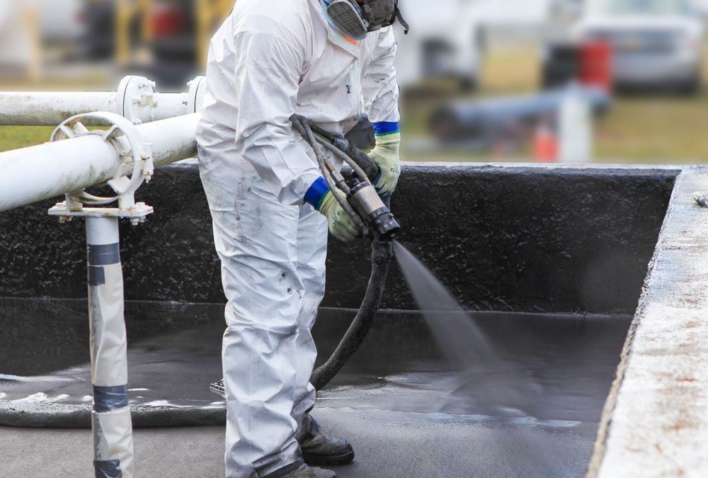 Person in protective suit spraying a black tank.