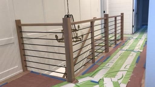 Staircase with light-toned carpeted steps, dark wooden handrails, and vertical black metal balusters.