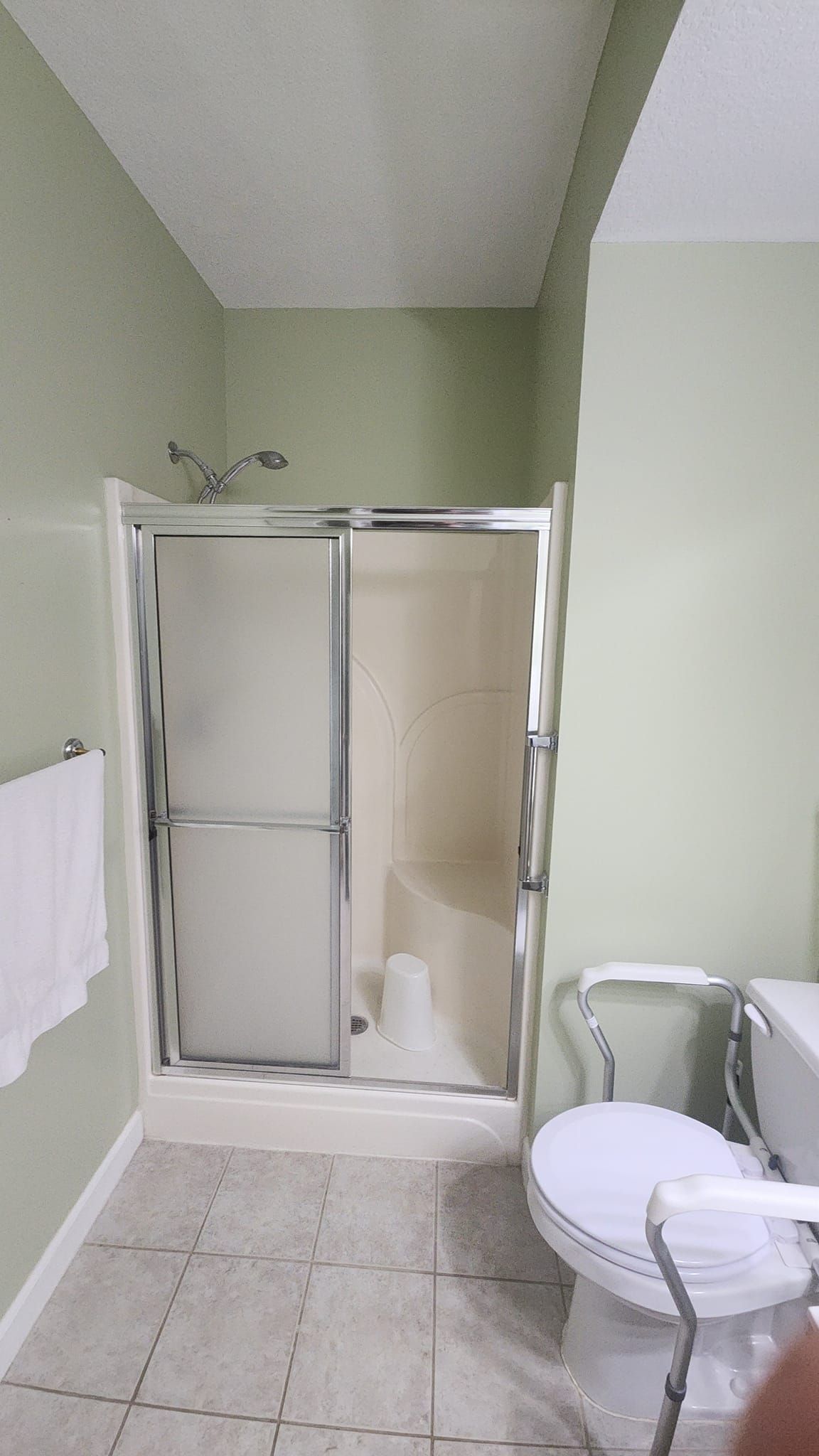 A bathroom featuring a shower stall with silver sliding glass doors and a white toilet with arm supports.