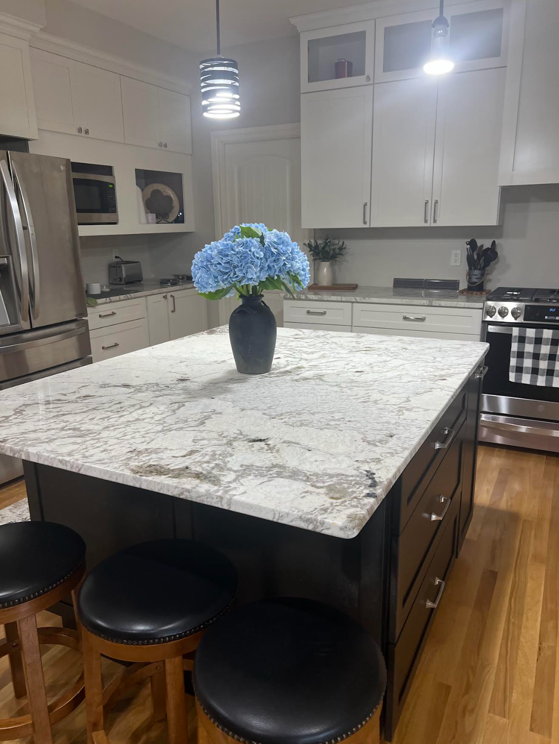A white kitchen with wood-look flooring, a central island, and a person standing by the counter under recessed lighting.