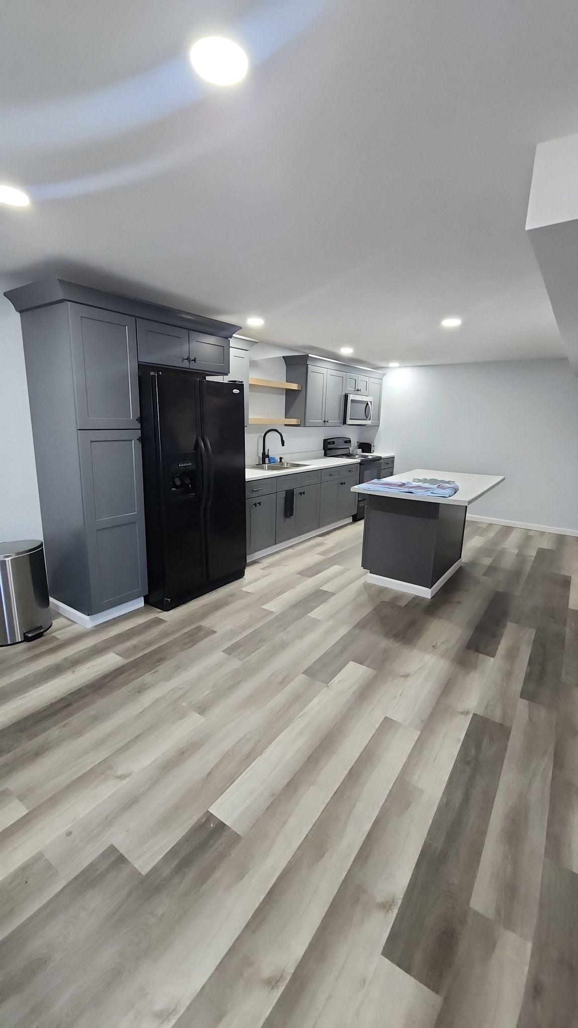 A modern kitchen featuring gray cabinets, black appliances, a central island, and wood-patterned flooring.