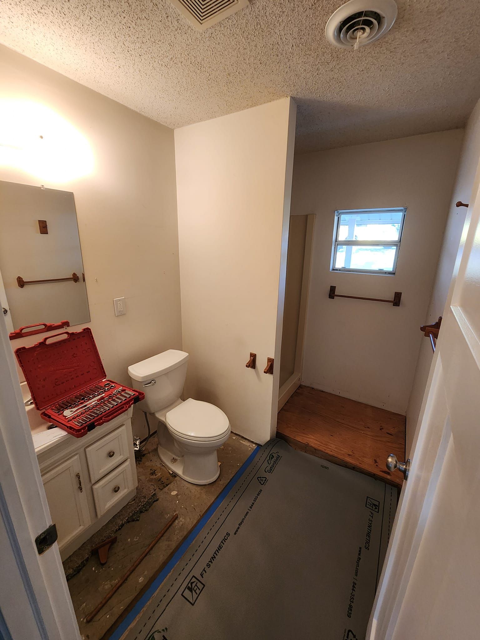 A partially renovated bathroom featuring a white vanity, a toilet, a red toolbox on the counter, and gray flooring.